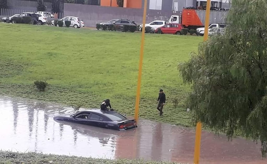 Pareja intenta cruzar desnivel inundado de plaza San Luis y su carro queda varado