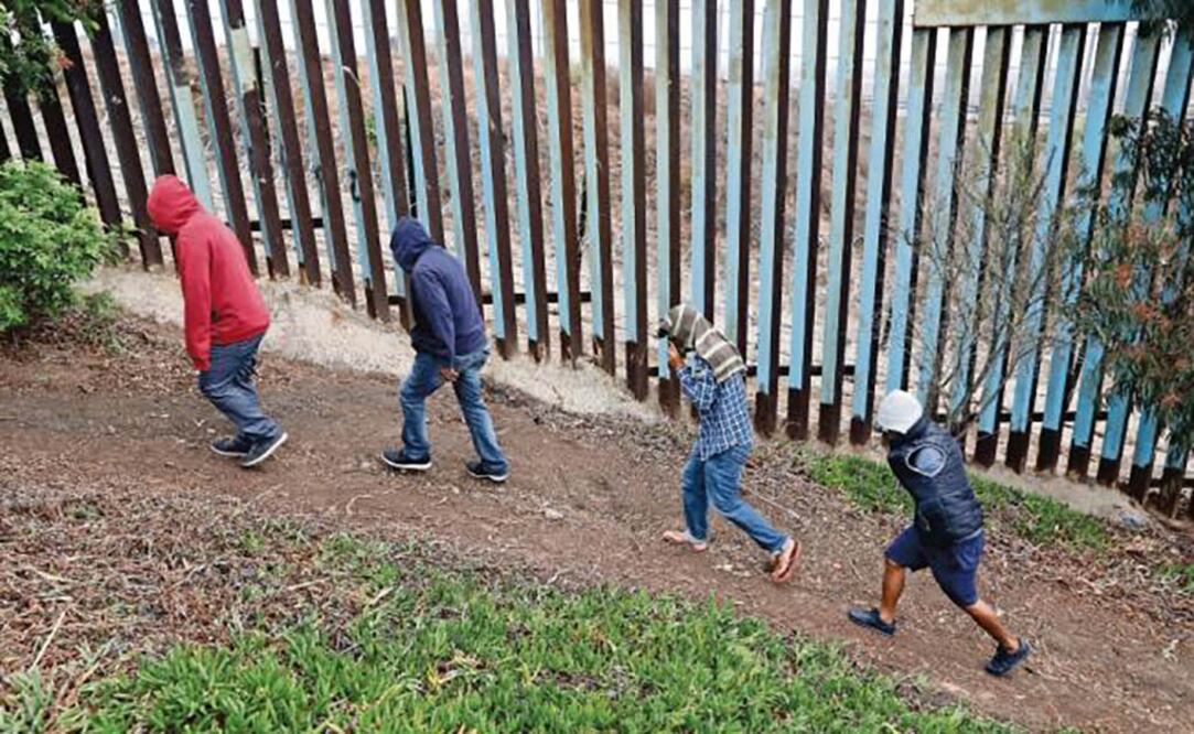 Migrantes caminan junto a una valla fronteriza en el crce entre Tijuana y Estados Unidos. (REBECCA BLACKWELL. AP)